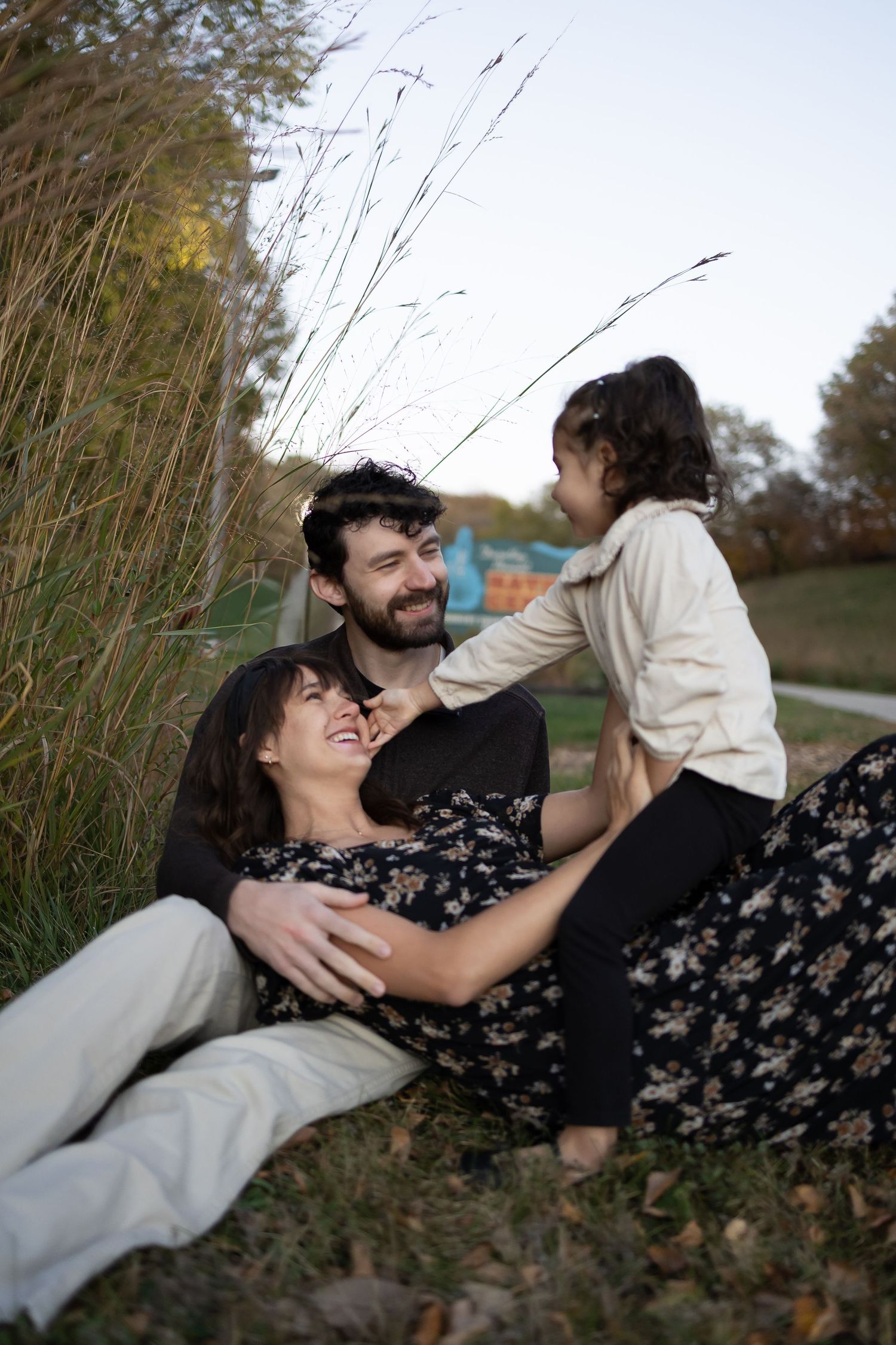 Sioux City, Iowa photographer. Joyful family of three relaxing and laughing together in an outdoor grassy park.