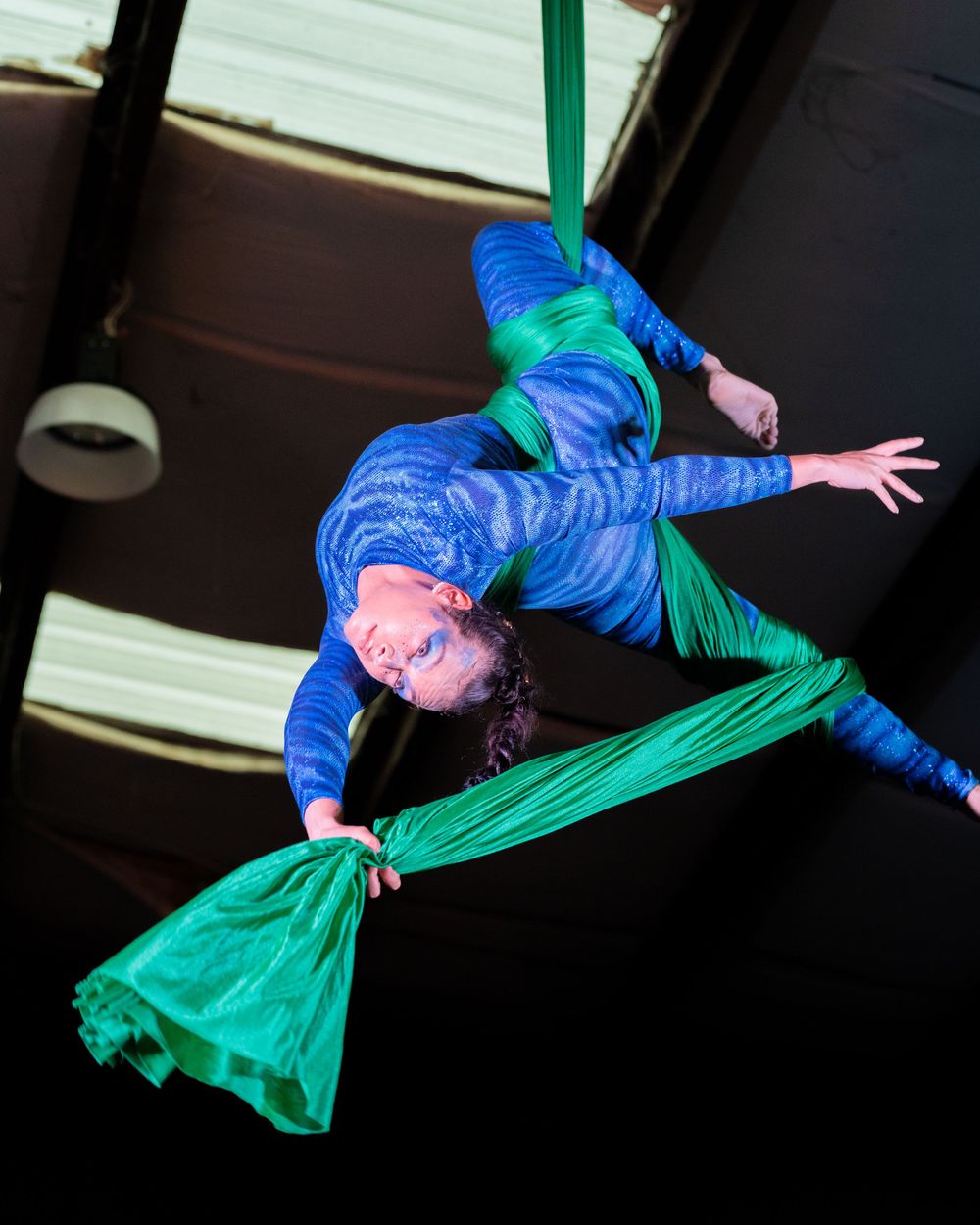 Aerial artist performing in blue and green costume on silk ribbons.