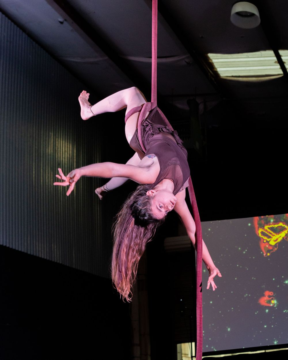 Aerial performer in pink costume spinning on silk fabric against dark background.