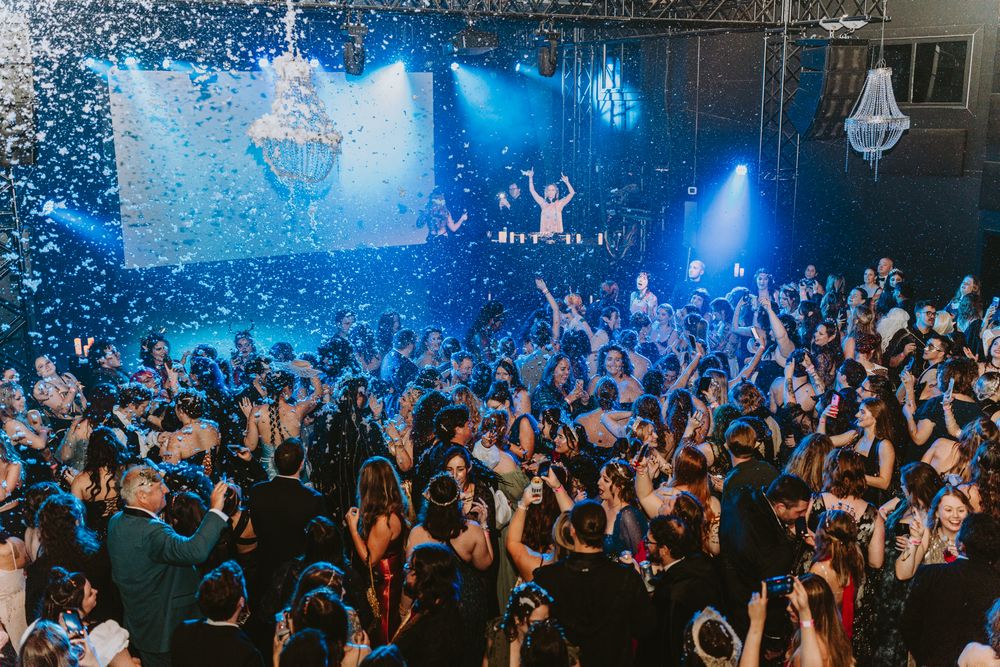 A crowded nightclub event with blue lighting and crystal chandeliers illuminating the dance floor.