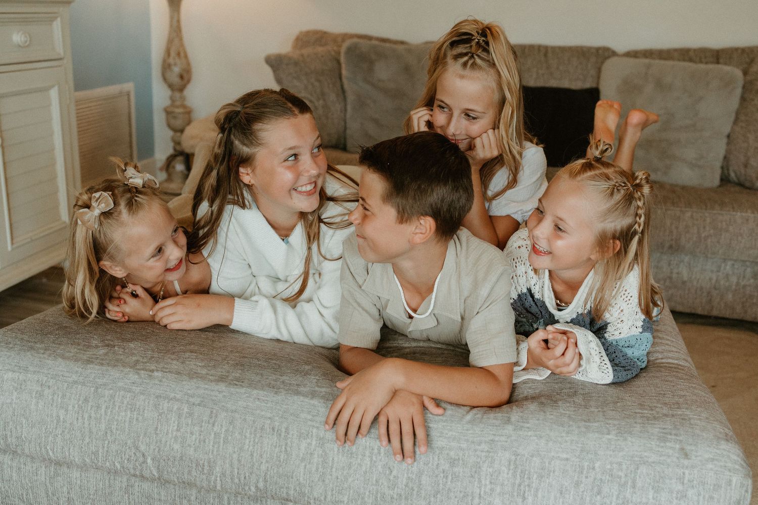 Family members lying down together on gray couch during casual indoor photo session.