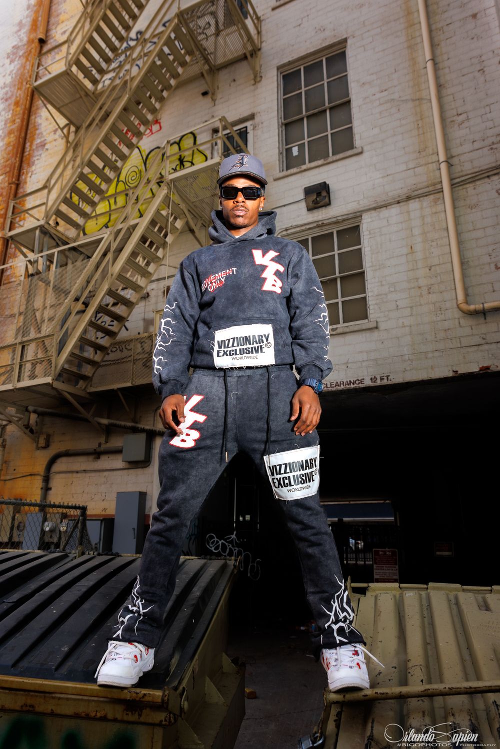 Urban fashion portrait of person in grey streetwear outfit on fire escape stairs.