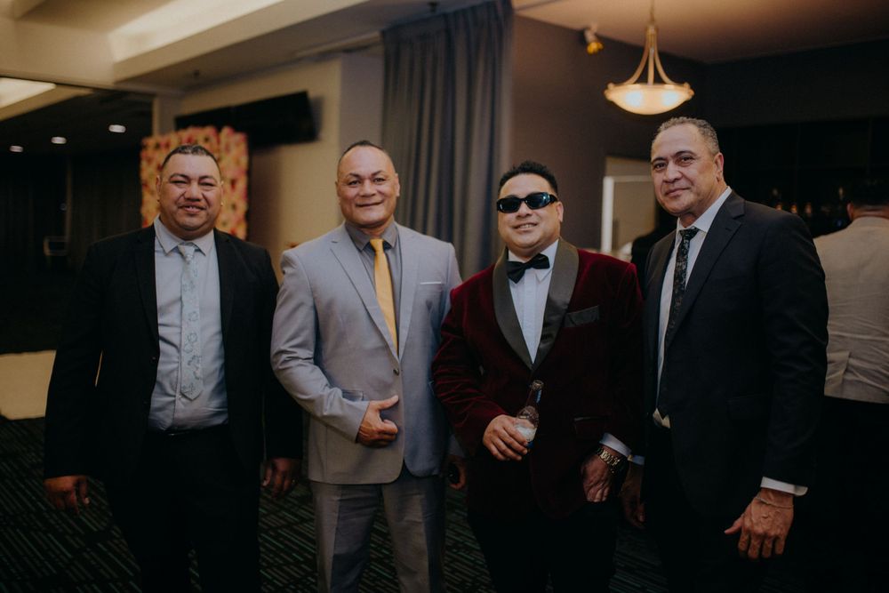 Four men in formal attire posing together at an indoor event or formal celebration.