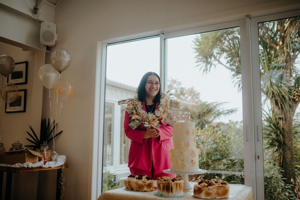Woman in pink dress holds floral arrangement near a cake display with balloons at an elegant indoor celebration.