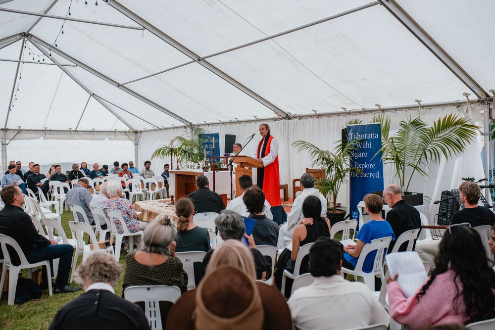 Guests seated under white marquee tent listening to speaker at an outdoor formal ceremony.