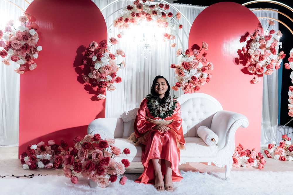Woman in pink dress sits on white sofa surrounded by pink and white floral arch decorations.