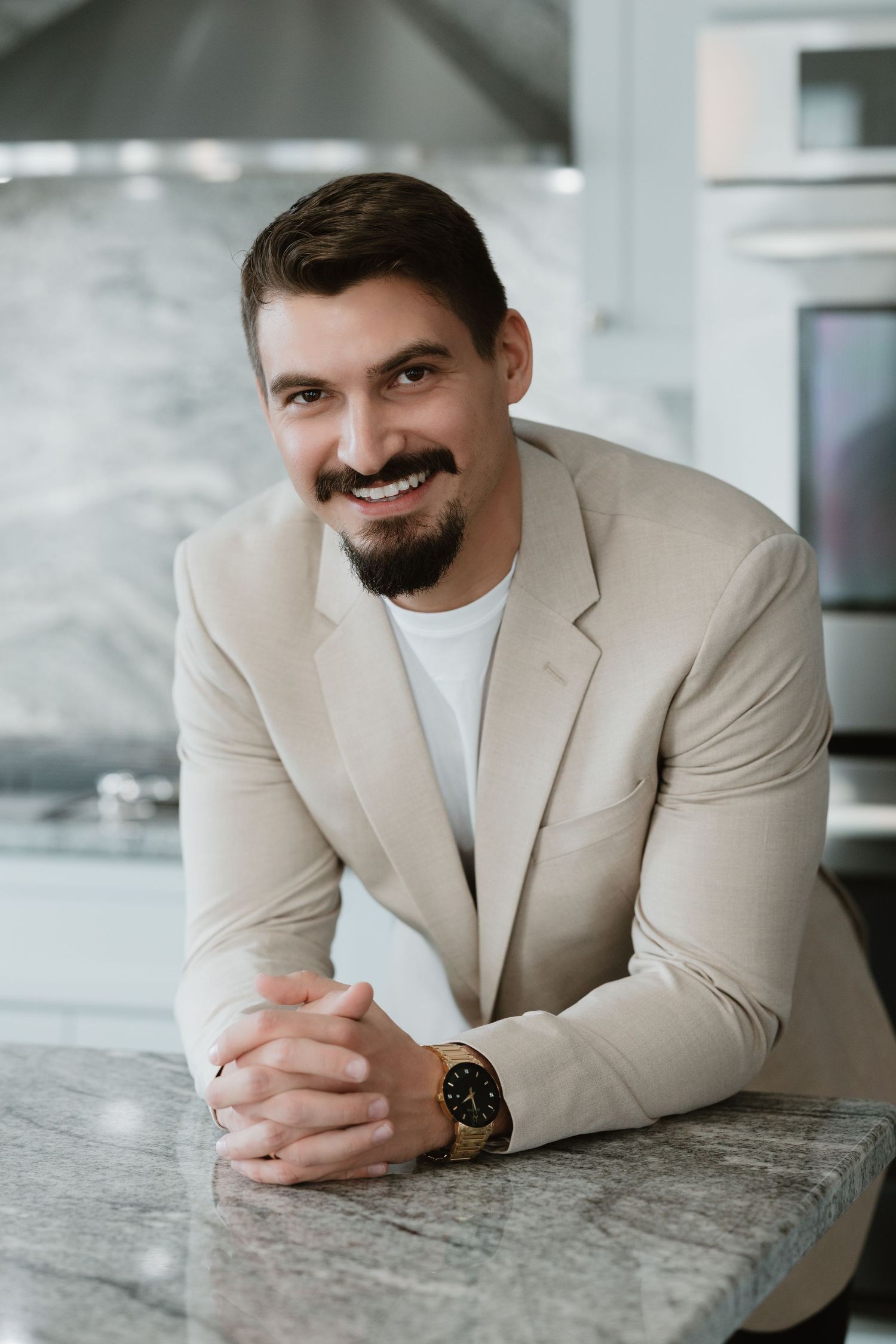 Professional headshot of realtor in beige blazer sitting at marble counter.