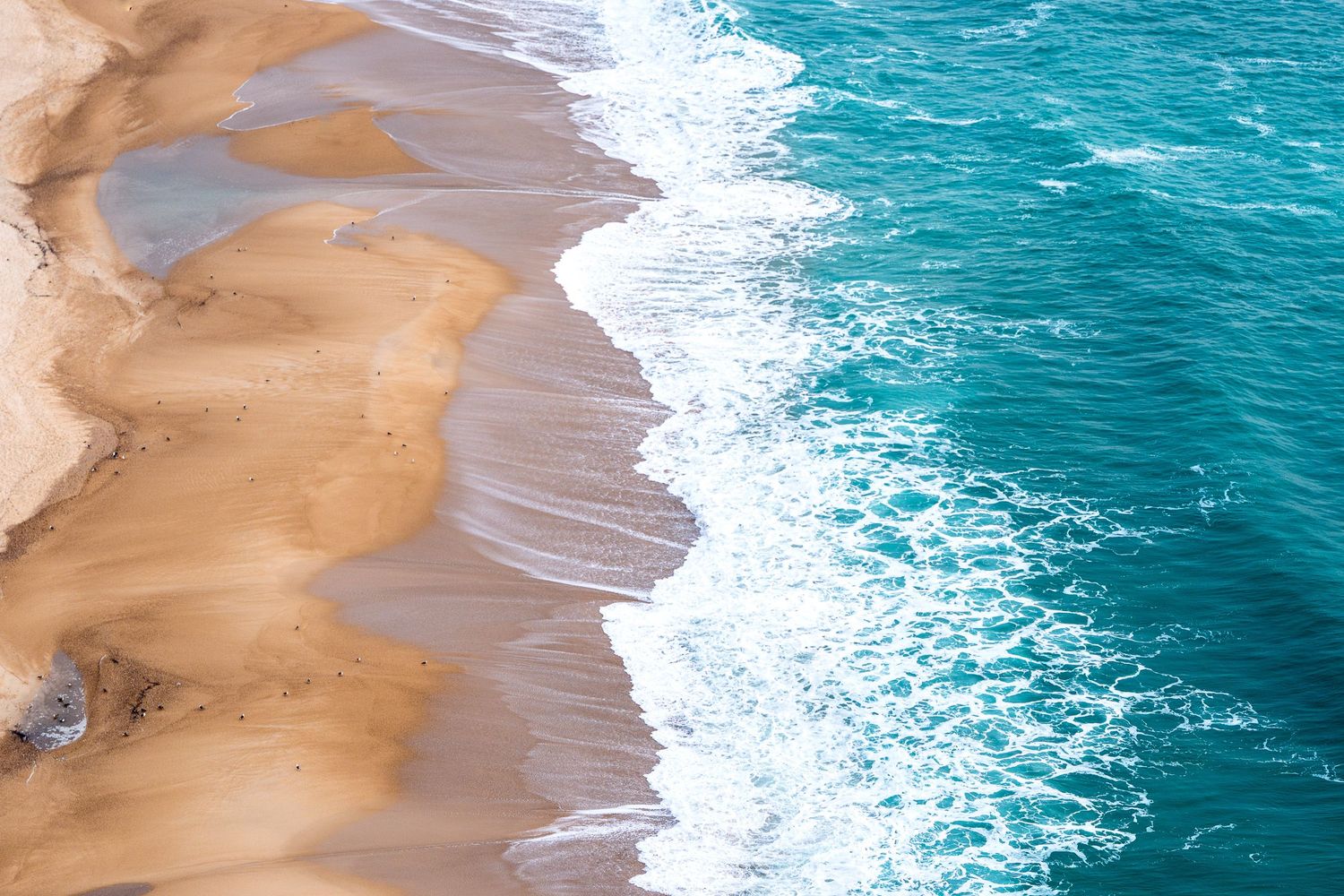 Aerial view of turquoise ocean waves gently washing onto a sandy beach shoreline.