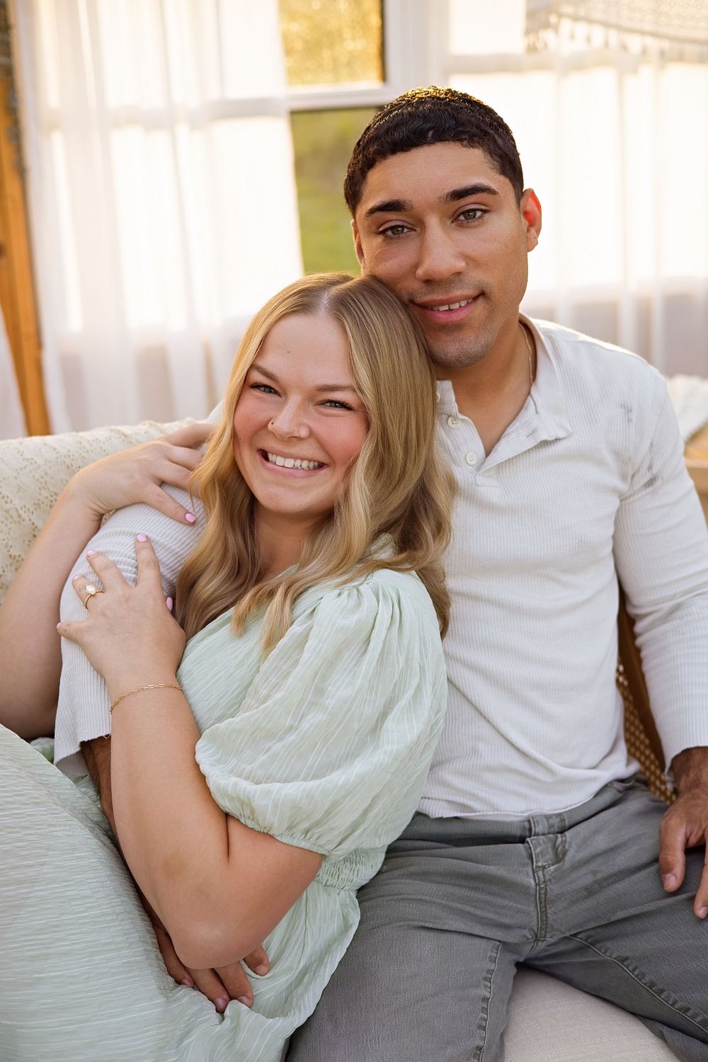 Happy couple sitting together on a couch, woman in mint dress smiling, man in white shirt embracing her warmly.