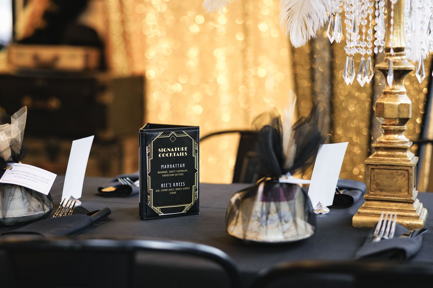 Elegant table setting with black tablecloth, vintage decor, and hanging crystals at formal event.