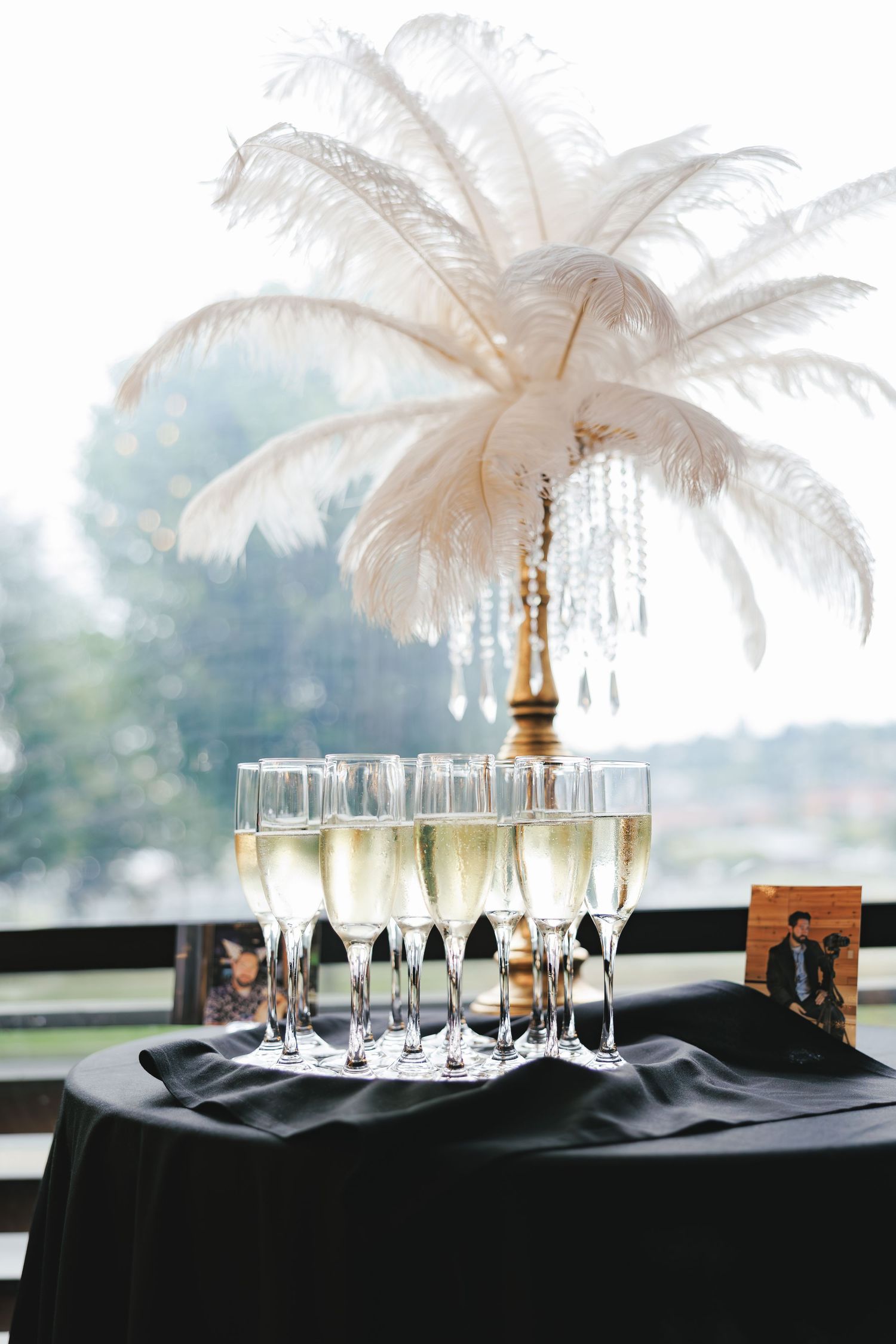 Elegant champagne display with white feather centerpiece on black tablecloth.