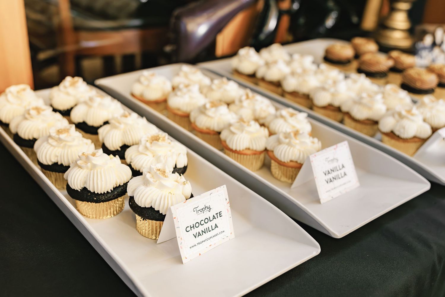 Three rows of frosted cupcakes displayed on white serving platters.