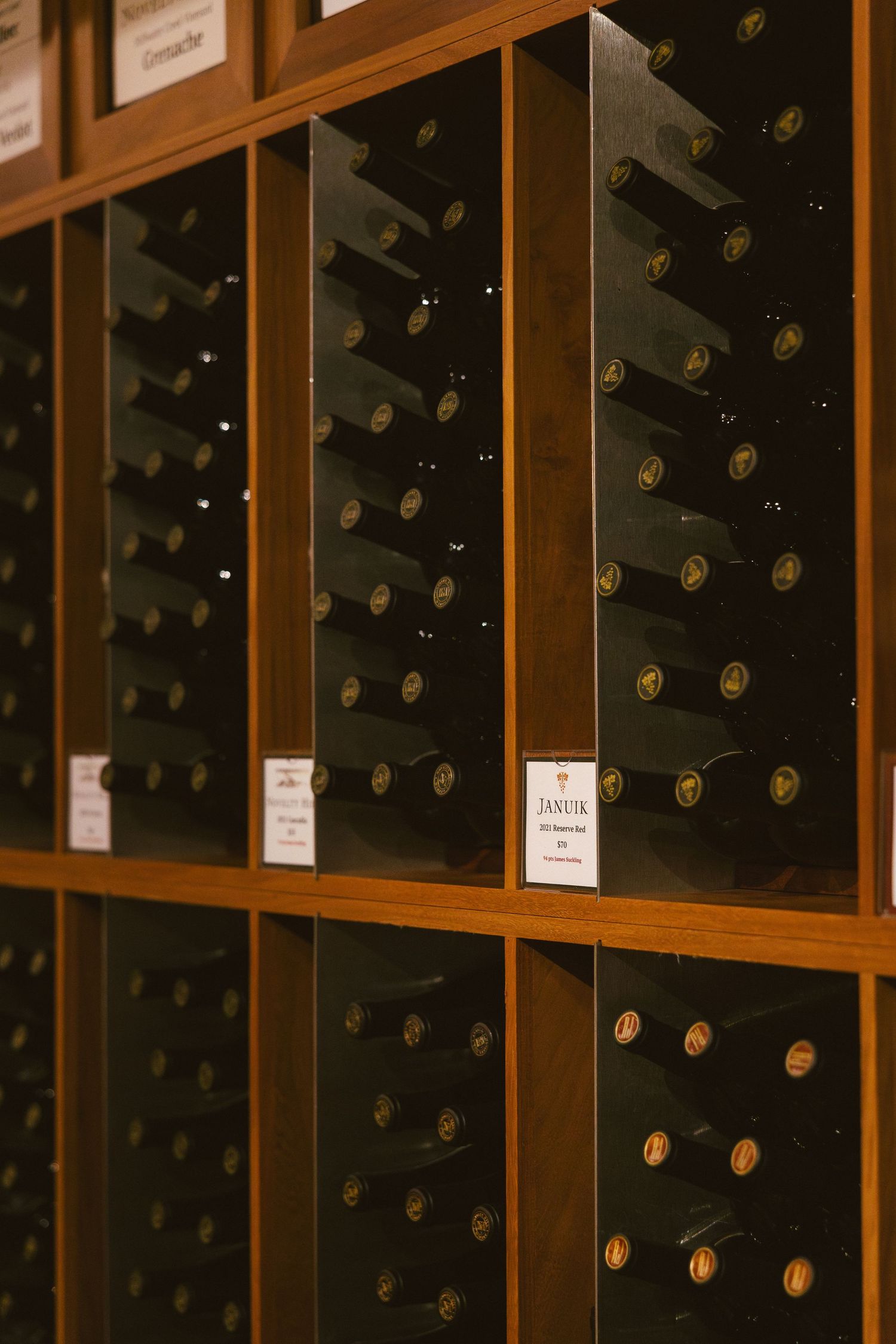 Wooden wine storage cubicles display organized rows of wine bottles stored horizontally in a wine shop.