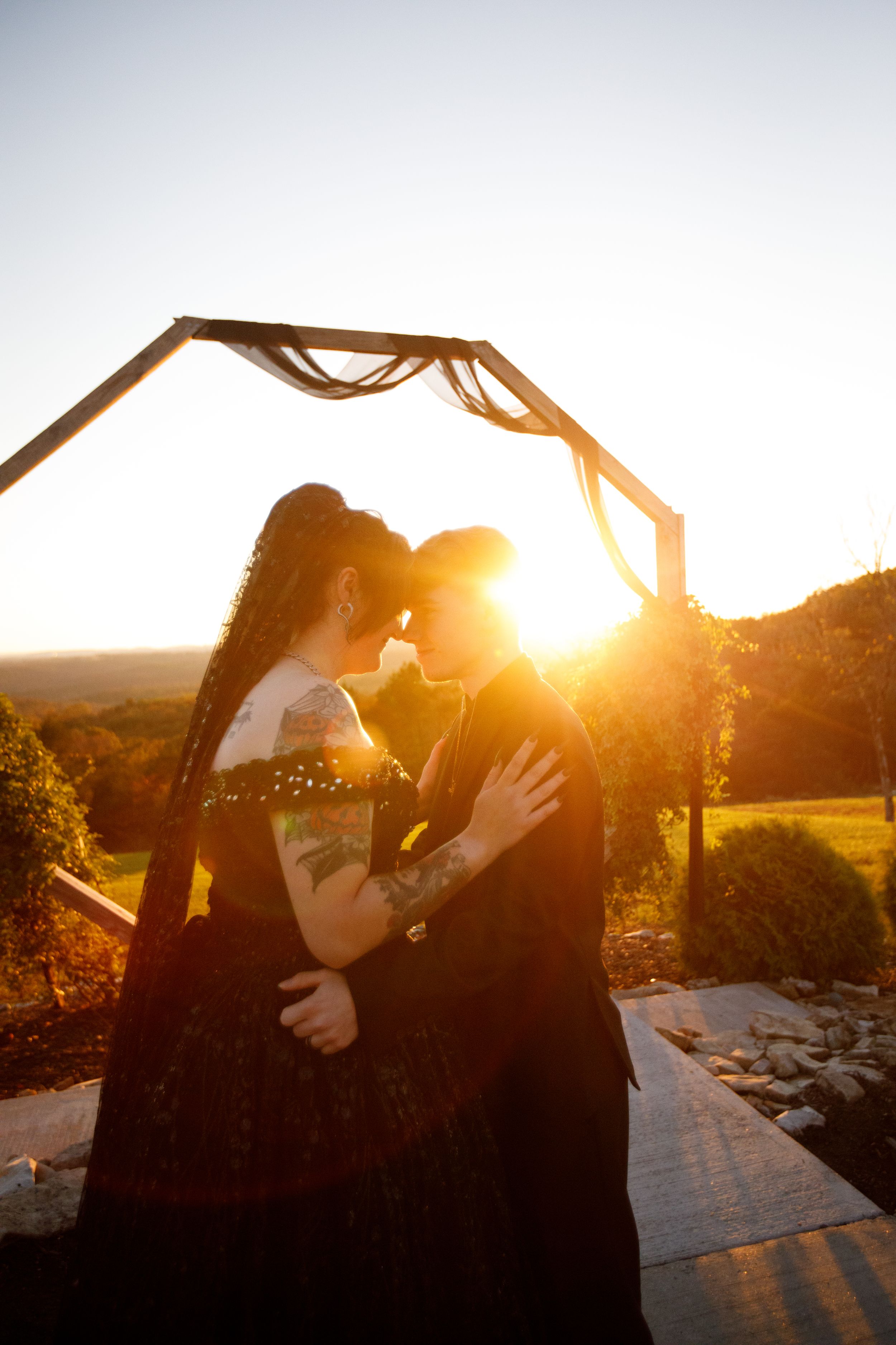 A couple shares an intimate moment under a wooden arch during golden hour sunset.