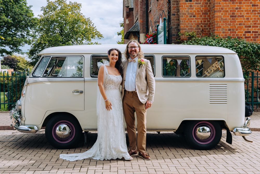 A classic white vintage VW bus serves as a wedding vehicle parked outside a brick building.
