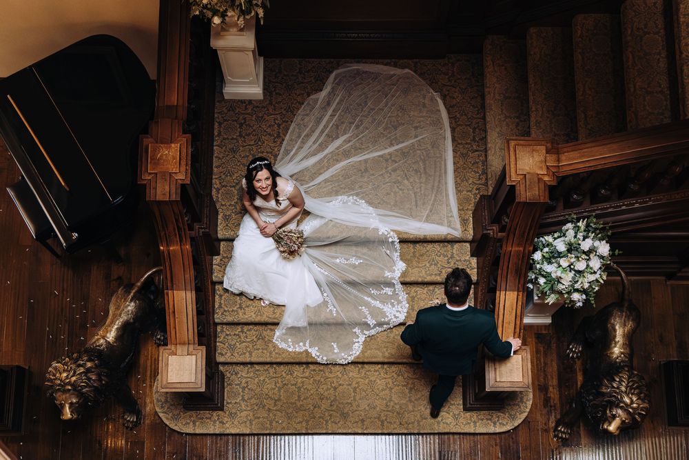 A bride in a white wedding dress lays on the floor in a grand architectural setting with dramatic lighting.
