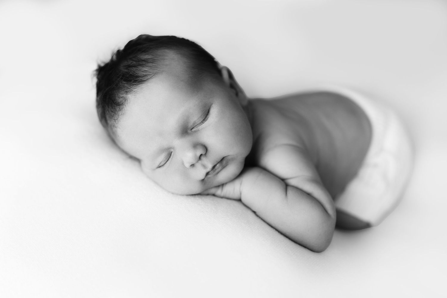 Black and white newborn baby sleeping peacefully curled up on a soft white blanket.