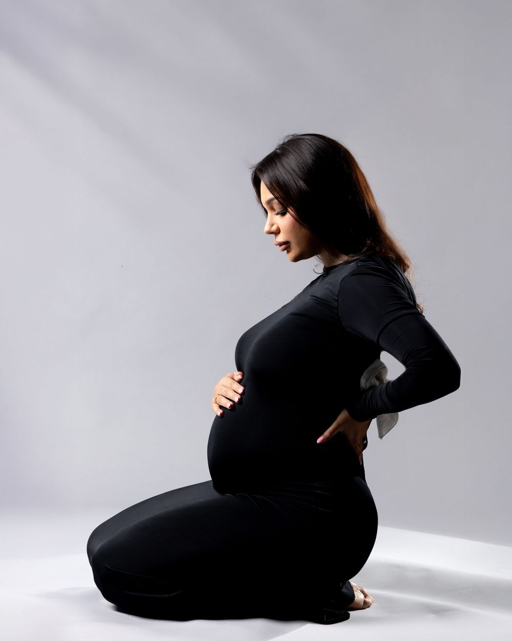 A figure in black clothing creates a minimalist silhouette against a white backdrop in a contemporary dance pose.
