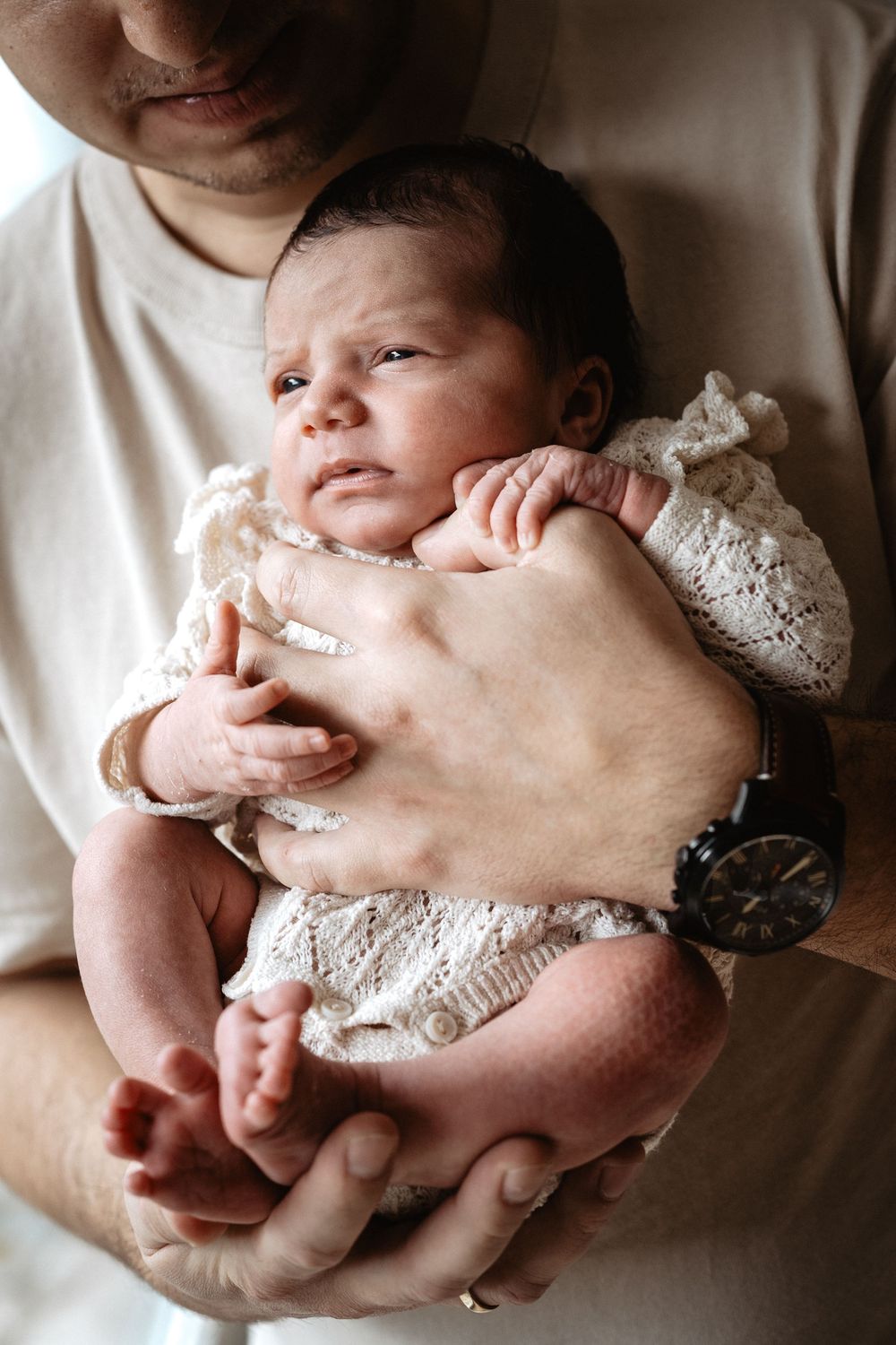 A series of intimate newborn photography shots showing a baby being gently cradled in arms wearing delicate lace clothing.