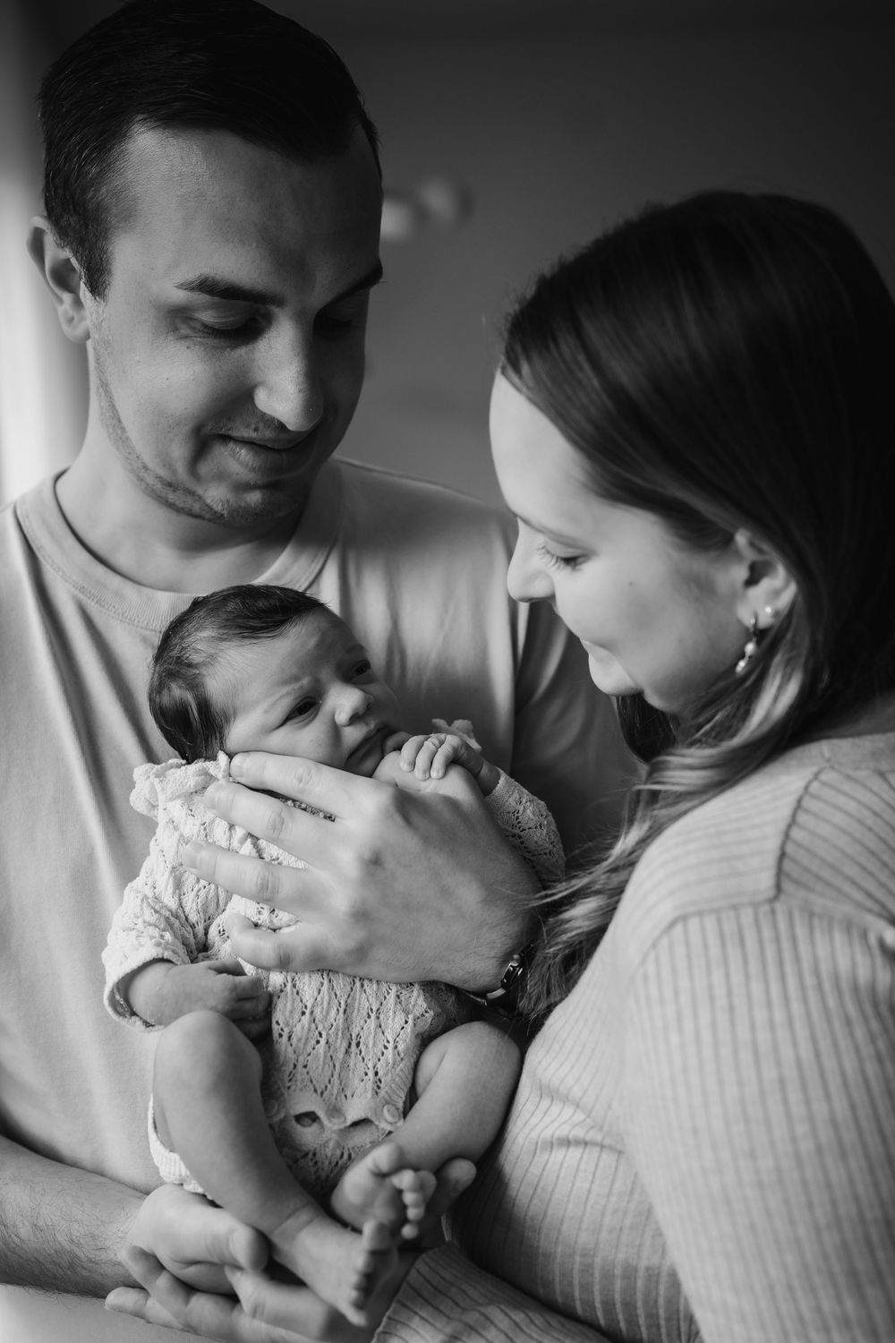 A black and white photo series showing tender moments between parents and their newborn baby in intimate close-ups.