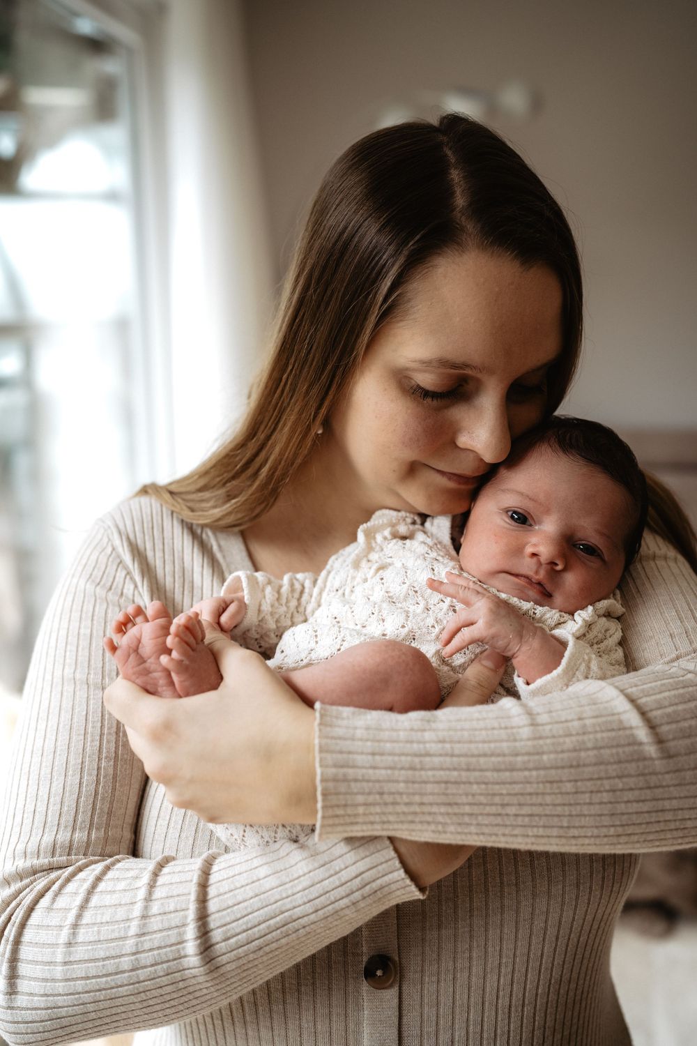 A tender series of photos showing a parent in a beige sweater cradling and kissing a newborn baby in white lace clothing.