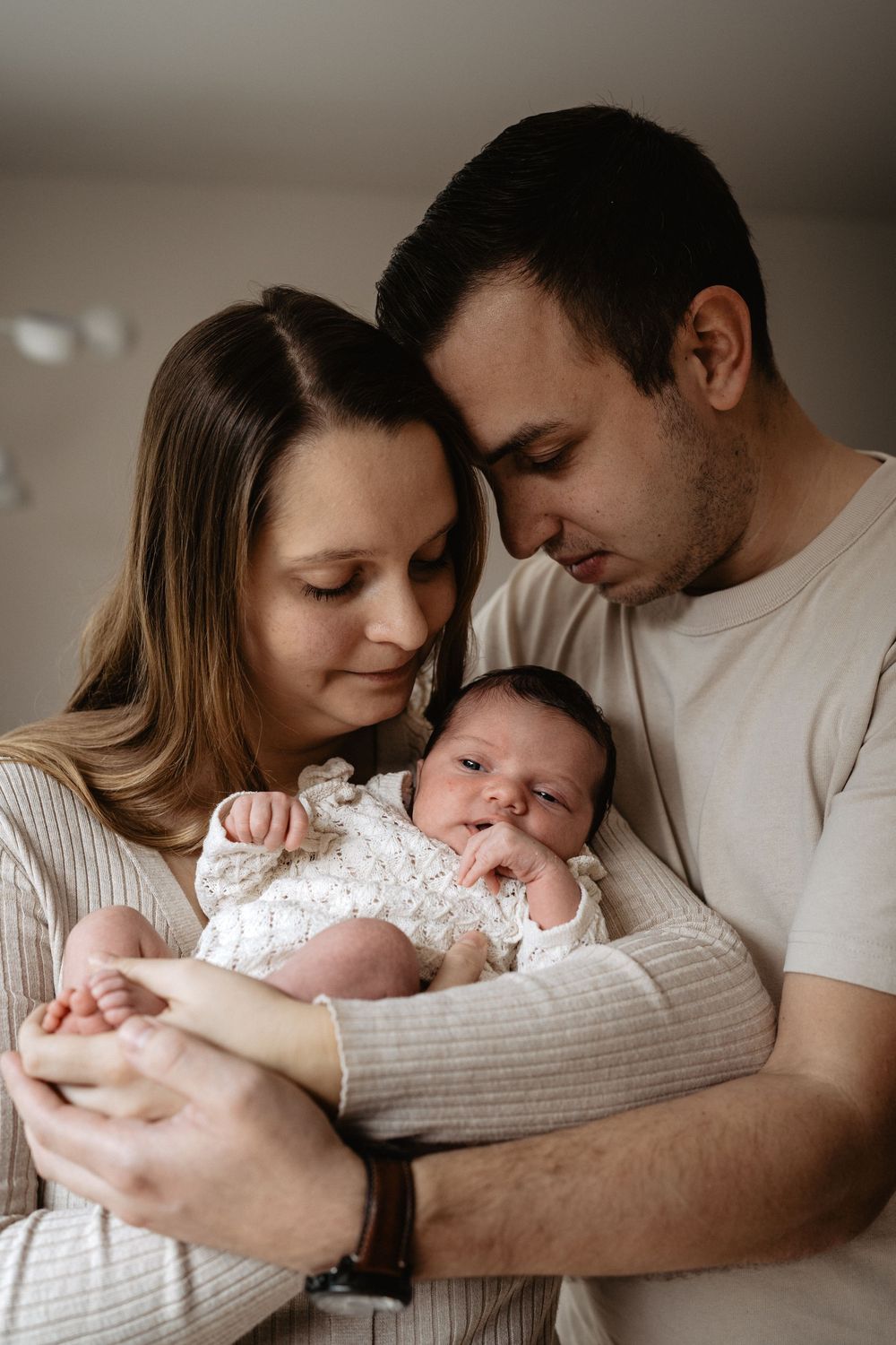 Intimate family photo series showing tender moments between parents and their newborn baby in soft natural light.