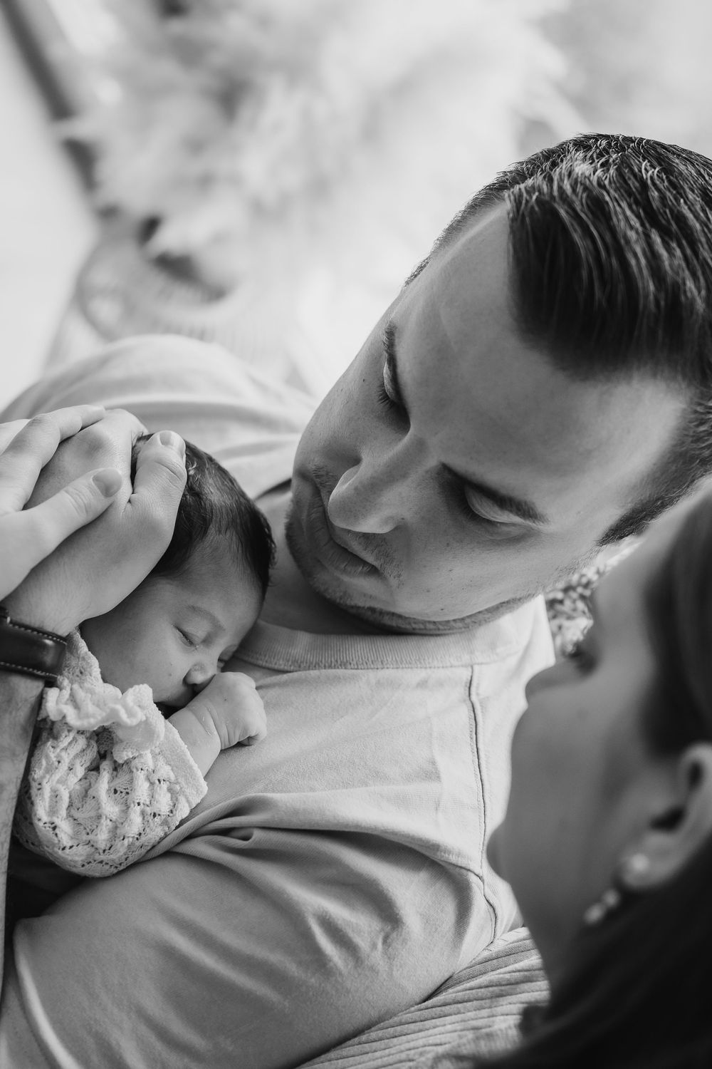 Black and white intimate photo of parents lovingly gazing at their sleeping newborn baby.