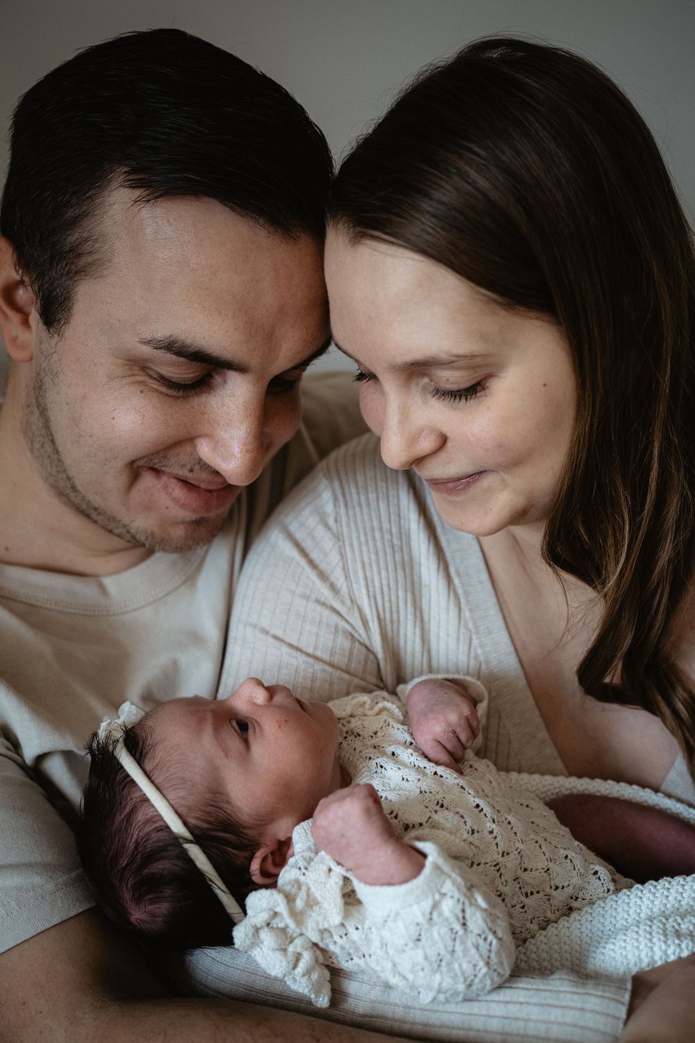 A tender series of intimate family moments showing parents gazing lovingly at their newborn baby in soft lighting.