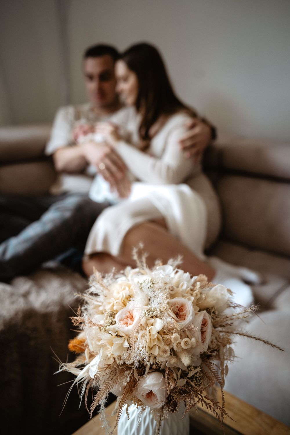 A romantic scene on a couch with a beautiful dried floral bouquet in cream and blush tones in the foreground.