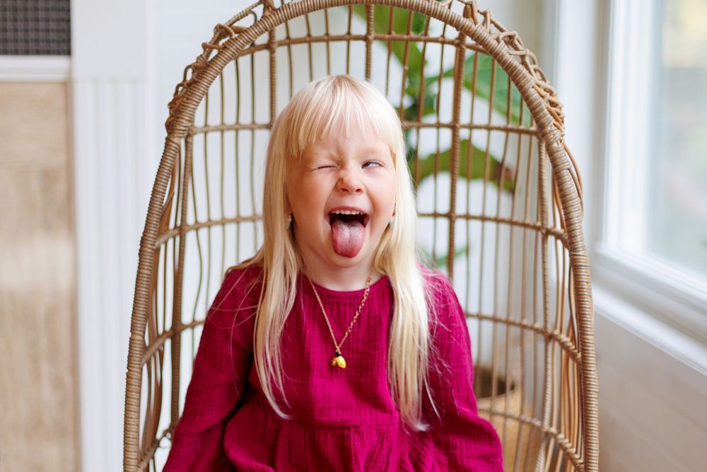 A series of five photos showing joyful expressions and reactions in a wicker chair by a window.