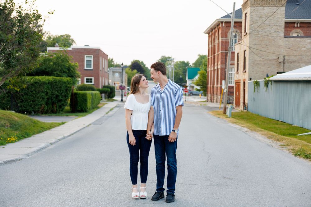 A couple walks hand in hand down a quiet suburban street on a sunny day.