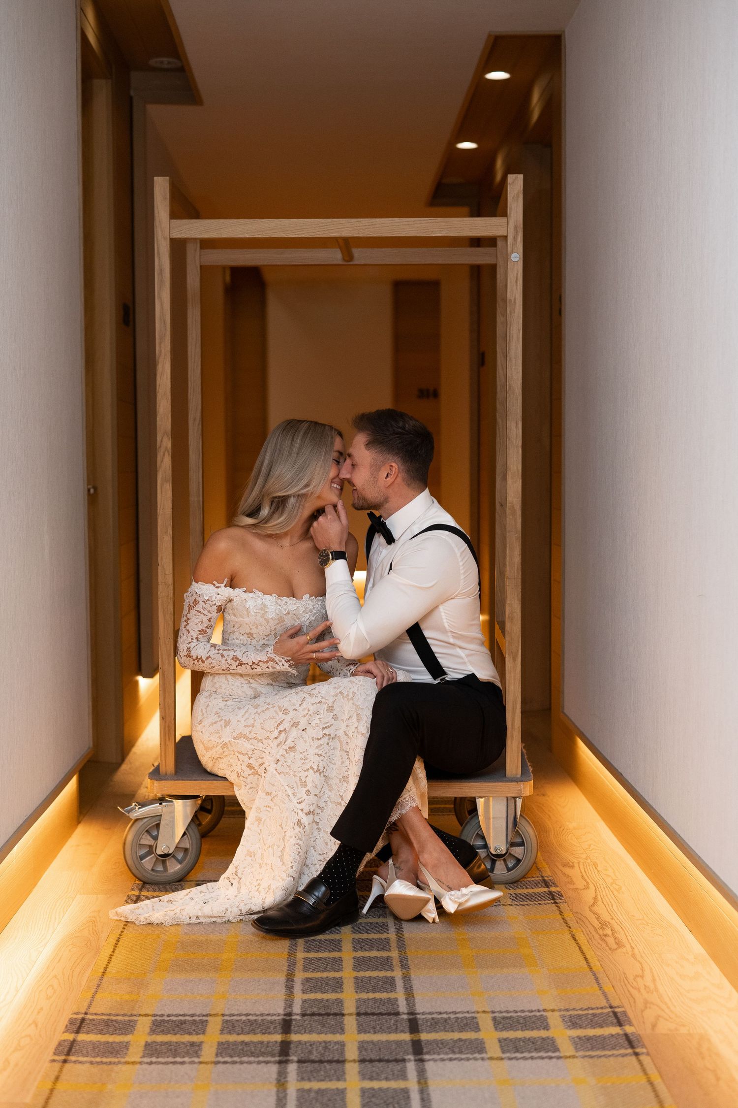 A couple in formal attire shares a romantic kiss while sitting in an illuminated hotel hallway. Royal Hotel Picton