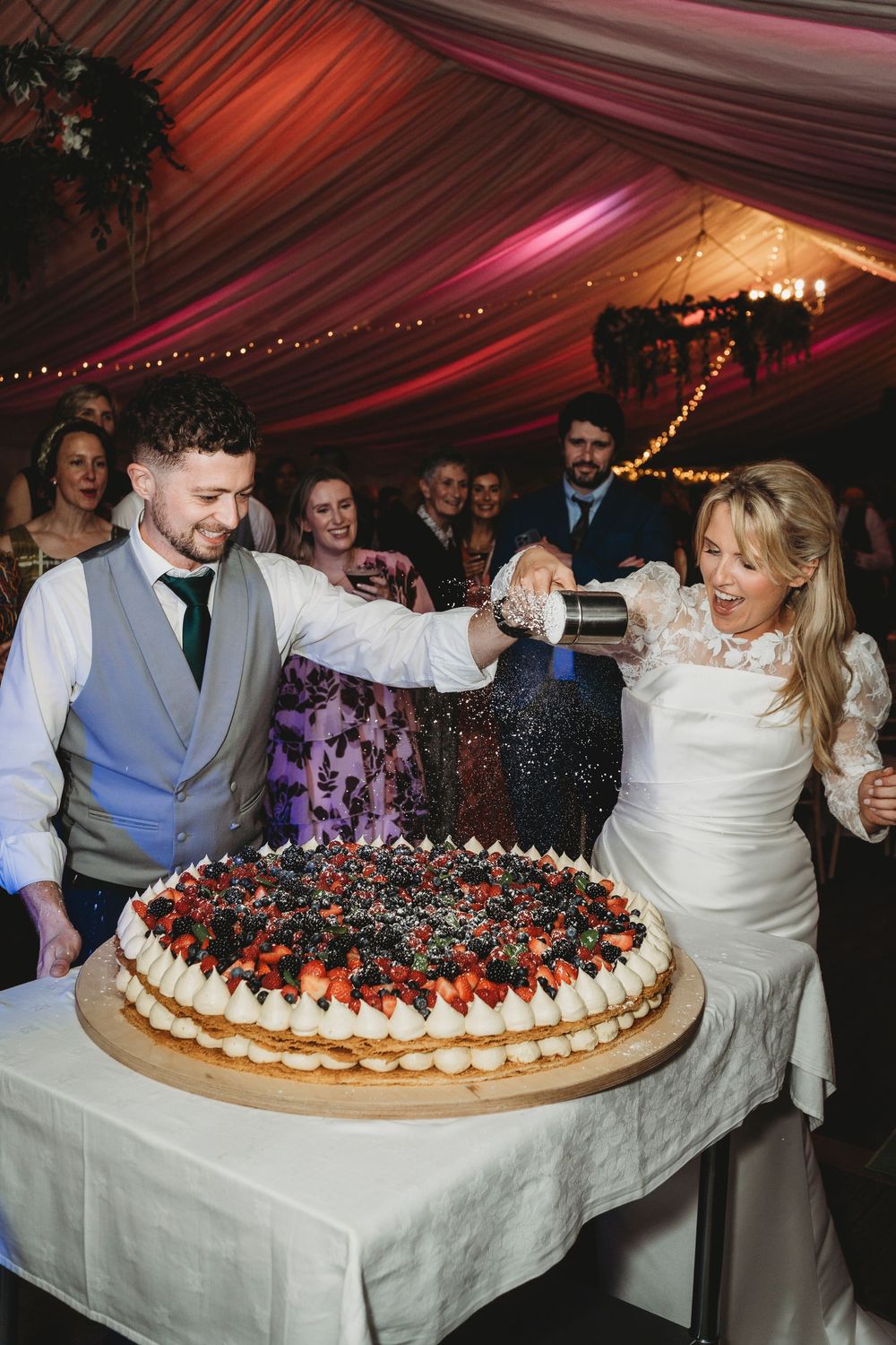 Bride and groom sprinkling flower over their enormous cake made by Crwst in Cardigan in the evening.