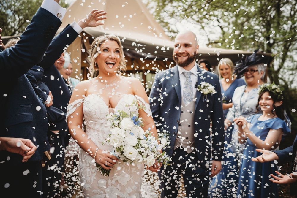 Couple walk out in confetti tunnel looking happy and in love