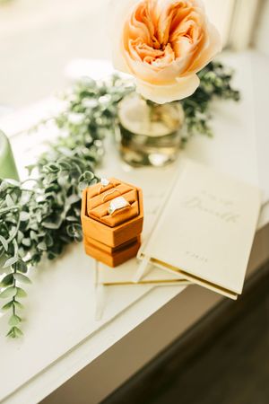 Wedding details with peach garden rose, eucalyptus and wooden ring box on white surface.