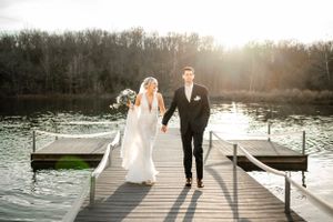 Couple walks along a white dock by the water during golden hour.