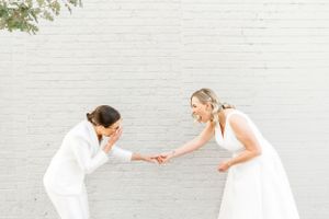 Playful interaction between two people in white attire against a white brick wall.