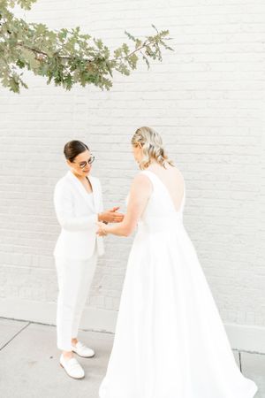 Joyful outdoor photo session with two people in all-white outfits near a brick wall.
