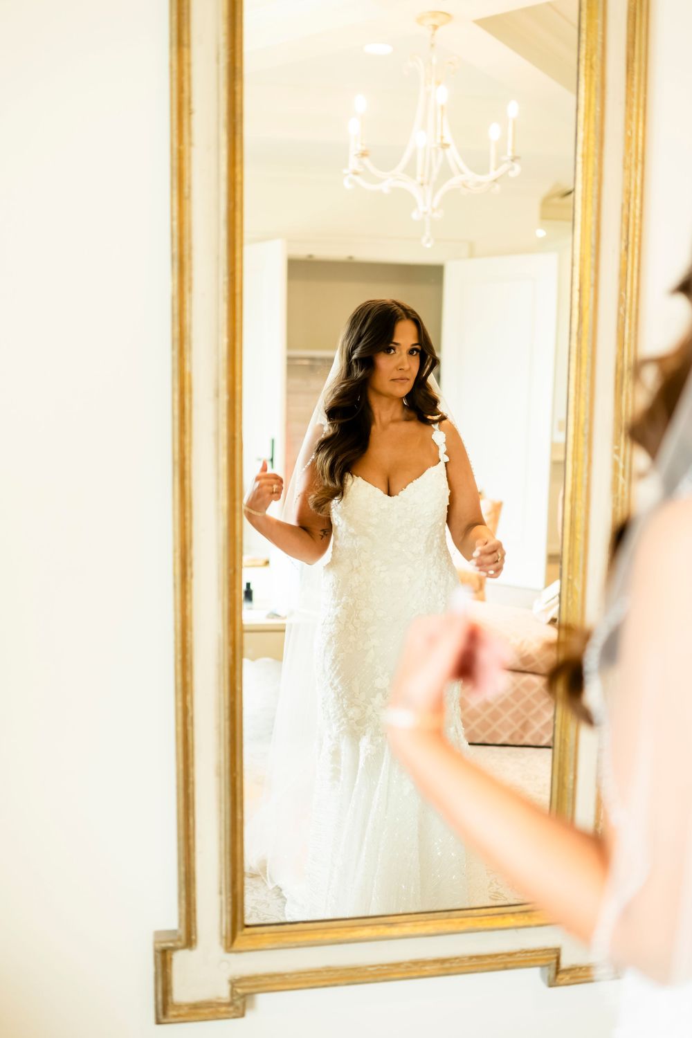 Elegant white wedding dress reflected in ornate gold-framed mirrors.