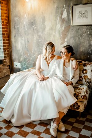 Two people in white formal attire sitting together on a vintage couch with checkered floor.