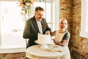 Newlyweds share an intimate moment in a rustic brick-walled venue with natural light streaming through windows.