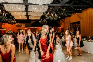 Wedding guests dance and celebrate on a rustic wooden dance floor under twinkling lights.