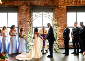 Wedding ceremony setup in an industrial-chic venue with exposed brick walls and large windows.