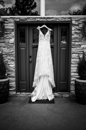 Wedding dress displayed against stone wall and dark doors in black and white photography.