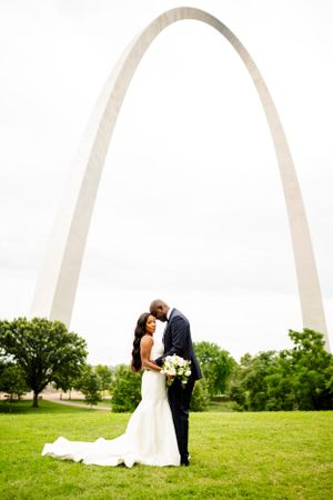 Romantic wedding portraits captured under the majestic St. Louis Arch on a green lawn.
