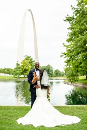 Wedding couple poses by a reflective pond with the St. Louis Arch in the background.