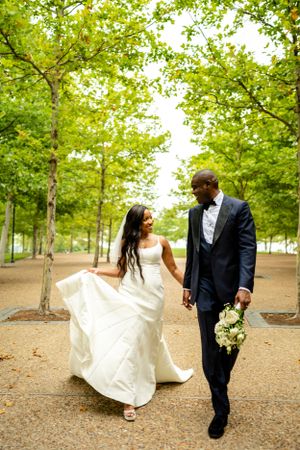 Wedding couple walks through a tree-lined path on a sunny day.