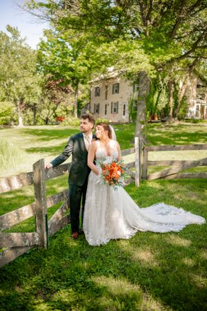 Newlyweds share romantic moment by rustic wooden fence in spring garden setting.