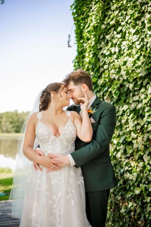 Romantic wedding couple embracing by ivy-covered wall in outdoor garden setting.