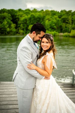 Newlyweds sharing romantic moment on wooden dock by serene lake.